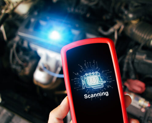Car Engine Scanning With Wireless Technical Tool, Obd2 Scanner Tool In A Mechanic Hand With A Car Engine Compartment Blurred On Background, Car Maintenance Service Concept
